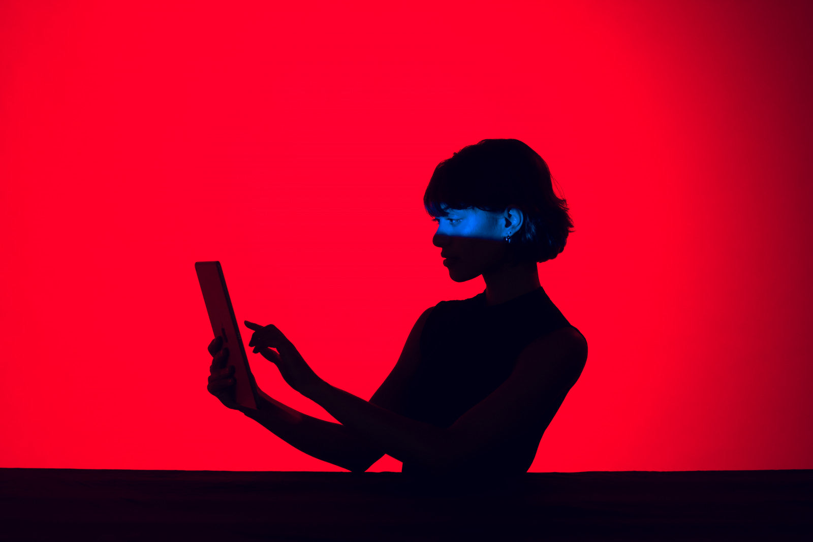 Silhouette of a person using a tablet, lit in blue against a bright red background