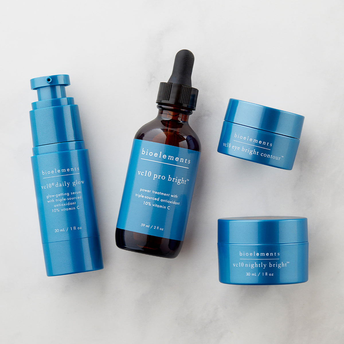 Four skincare products from bioelements arranged on a light gray marble background: a blue pump bottle, an amber dropper bottle with a black dropper cap, and two blue jars with black lids. The central dropper bottle is labeled 'bioelements ve10 pro bright' and the others are labeled with similar names.